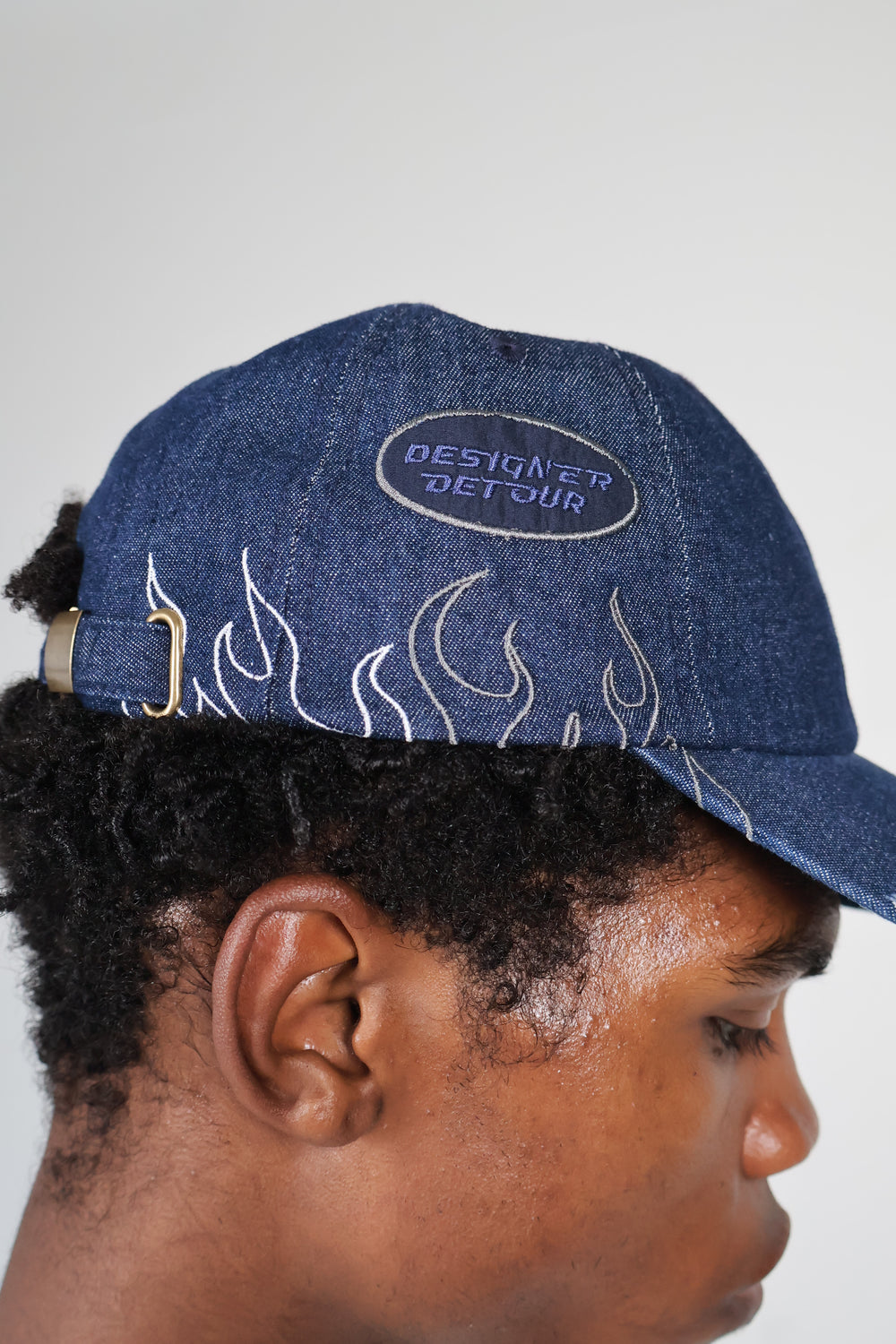Model wearing dark denim baseball cap with flame embroidery and "DESIGNER DETOUR" patch, paired with white streetwear sweatshirt featuring bold "DRIP KIT" logo – modern urban fashion look, unisex edgy cap styling, premium streetwear brand photography.

 baseball millennials couples streetwear style fashion sustainable eco-friendly vacation daily essentials Gen Z cap hat bold statement luxury cool summer clothing trend outfit OOTD Instagram designer dripkit eco-fashion streetwear 
