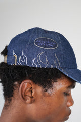 Model wearing dark denim baseball cap with flame embroidery and "DESIGNER DETOUR" patch, paired with white streetwear sweatshirt featuring bold "DRIP KIT" logo – modern urban fashion look, unisex edgy cap styling, premium streetwear brand photography.

 baseball millennials couples streetwear style fashion sustainable eco-friendly vacation daily essentials Gen Z cap hat bold statement luxury cool summer clothing trend outfit OOTD Instagram designer dripkit eco-fashion streetwear 
